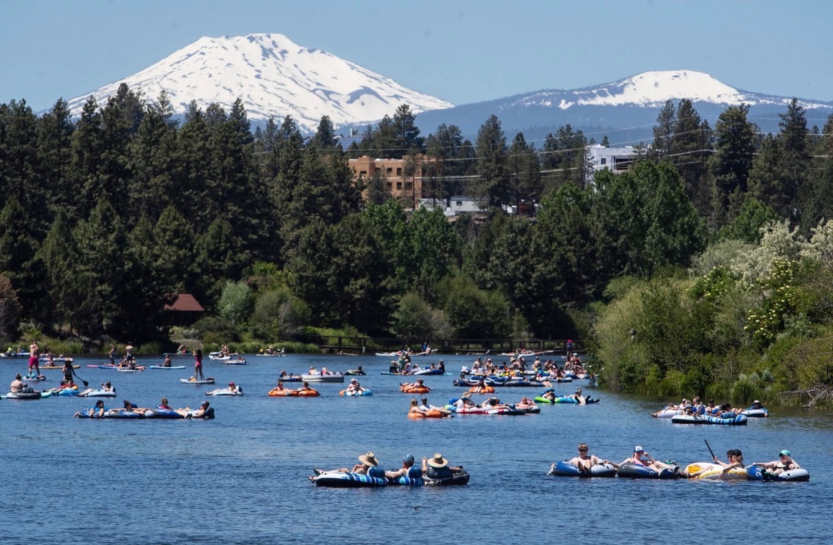 Tubers and paddleboarders floating the Deschutes River in Bend with Mt. Bachelor behind
